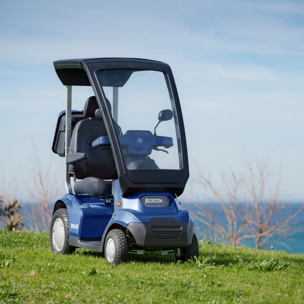 Afiscooter S4 Solar mobility scooter with a canopy on a grassy hill near the ocean.
