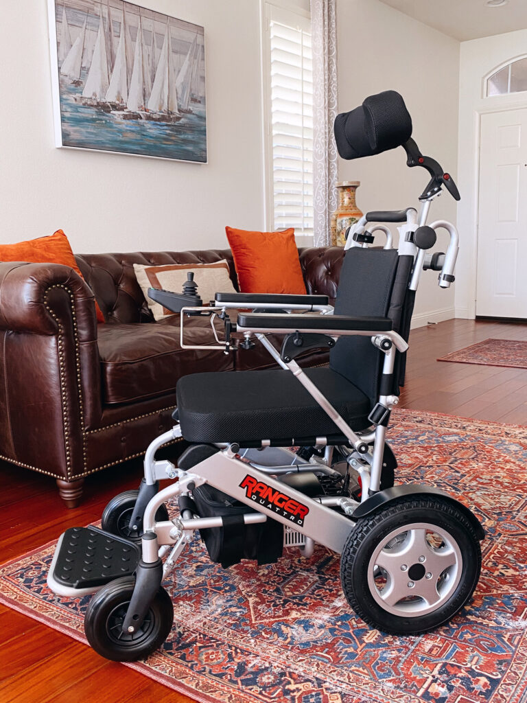 Porto Mobility Ranger Quattro folding power wheelchair with headrest in a living room beside a leather sofa
