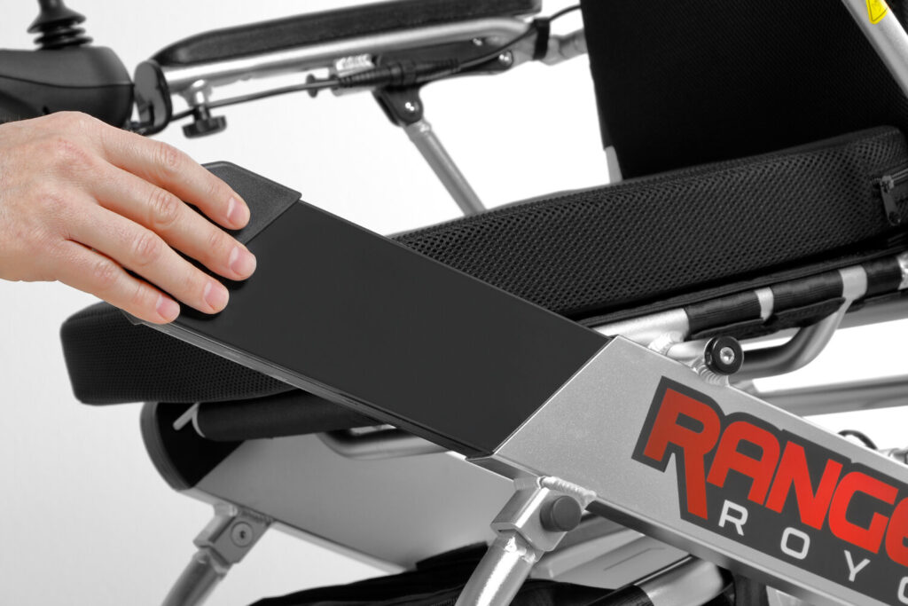 Porto Mobility Ranger Royce folding power wheelchair, hand sliding a flat pack into the frame beside the seat
